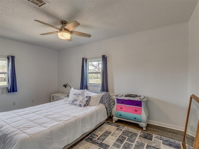 bedroom featuring a textured ceiling, wood finished floors, multiple windows, and visible vents