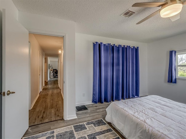 bedroom with baseboards, a textured ceiling, visible vents, ceiling fan, and wood finished floors