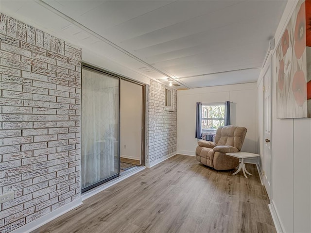 sitting room featuring brick wall, baseboards, and wood finished floors