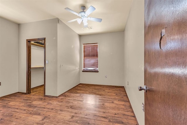 unfurnished bedroom with visible vents, a closet, ceiling fan, a walk in closet, and wood finished floors