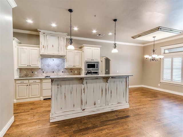 13340 Greenscape Rd, Piedmont, OK 73078 - kitchen featuring decorative backsplash, a center island with sink, stainless steel microwave, and ornamental molding