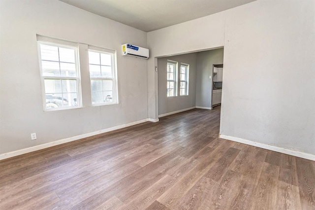 spare room with a wall unit AC, wood finished floors, and baseboards