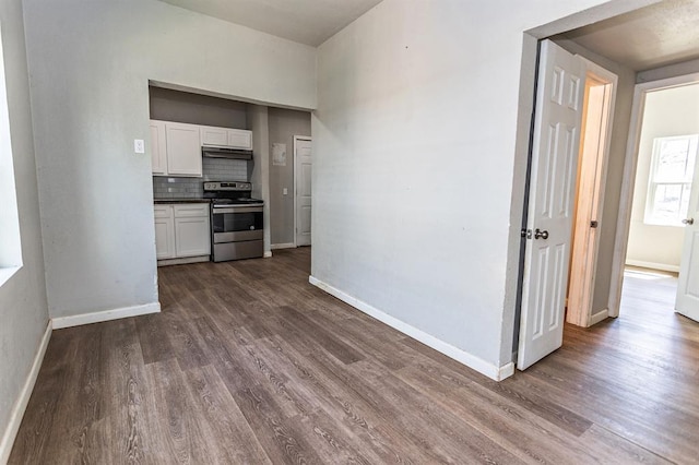 interior space featuring stainless steel range with electric cooktop, dark wood finished floors, white cabinets, under cabinet range hood, and baseboards