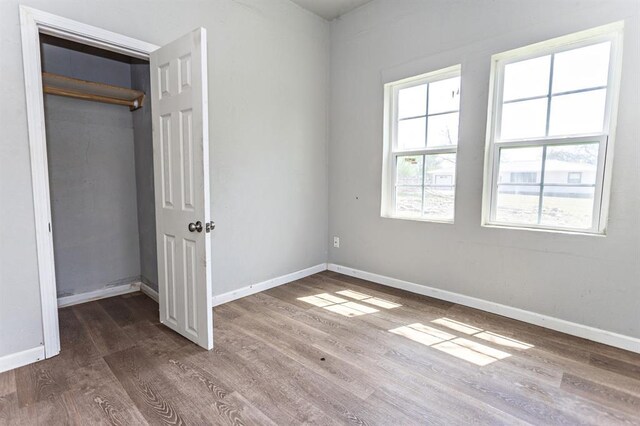 unfurnished bedroom featuring wood finished floors, baseboards, and a closet