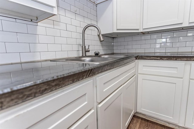 kitchen featuring white cabinetry, dark stone countertops, dark wood-style flooring, a sink, and decorative backsplash