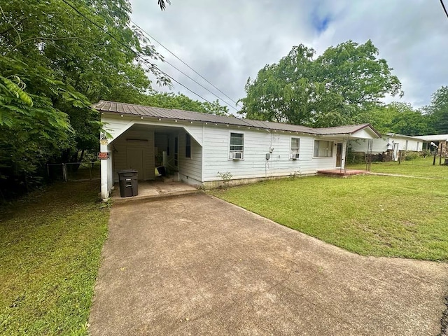 back of property featuring concrete driveway, fence, metal roof, a yard, and a carport