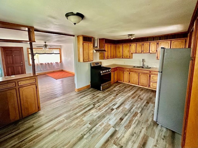 kitchen featuring a sink, stainless steel gas range oven, light wood finished floors, freestanding refrigerator, and a ceiling fan