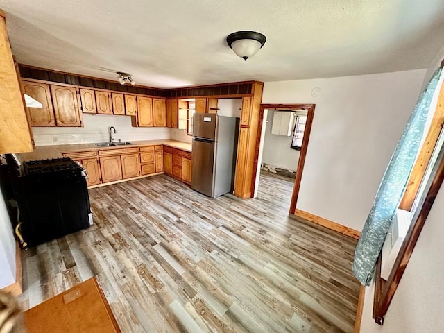 kitchen with freestanding refrigerator, light wood-style floors, gas range oven, light countertops, and a sink