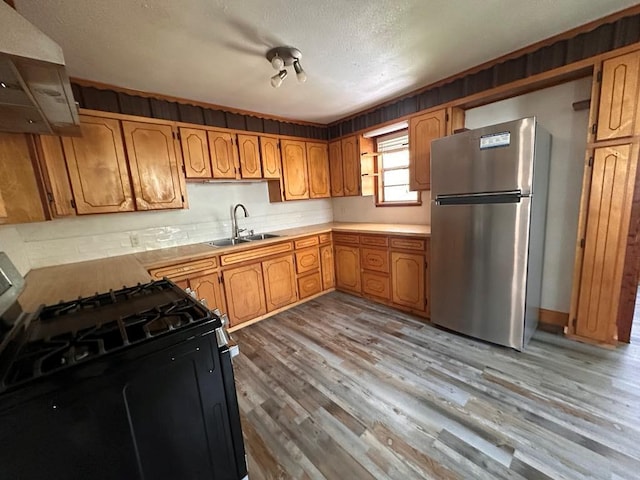 kitchen featuring freestanding refrigerator, extractor fan, a sink, light wood finished floors, and black range with gas cooktop