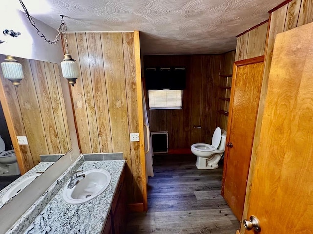 bathroom featuring wooden walls, vanity, toilet, and wood finished floors