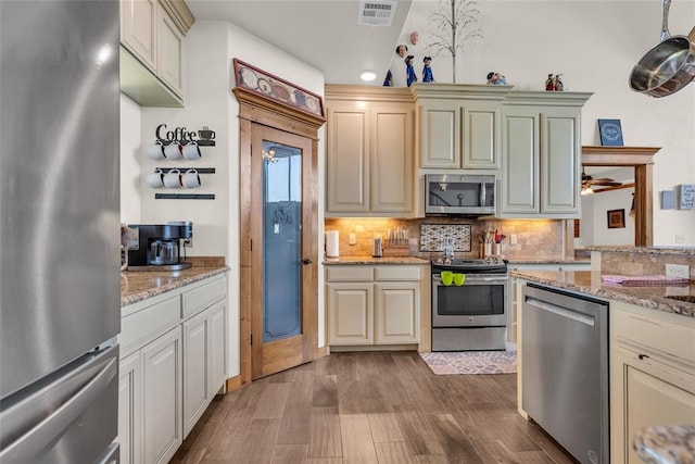 kitchen with tasteful backsplash, visible vents, wood finished floors, light stone counters, and stainless steel appliances