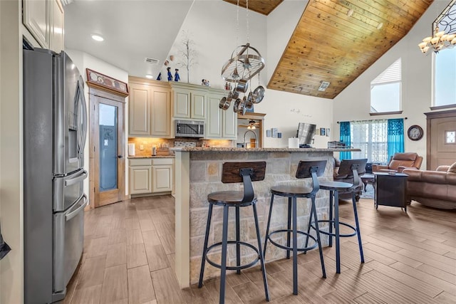 kitchen featuring open floor plan, a chandelier, a kitchen bar, stainless steel appliances, and high vaulted ceiling