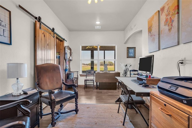office area with wood finished floors, visible vents, and a barn door