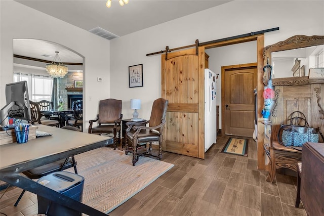 home office featuring wood finished floors, an inviting chandelier, visible vents, and a barn door