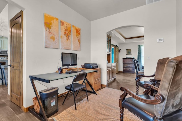 office space with arched walkways, a raised ceiling, baseboards, and wood finished floors