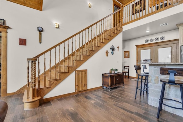 staircase with a high ceiling, wood finished floors, baseboards, and visible vents