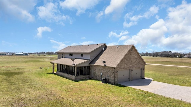 exterior space featuring concrete driveway, roof with shingles, an attached garage, a yard, and a sunroom