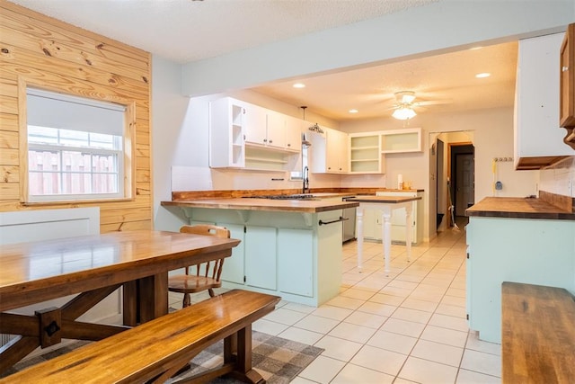 515 W Tennessee Ave, Pauls Valley, OK 73075 - kitchen with open shelves, wooden counters, a peninsula, light tile patterned floors, and a breakfast bar area