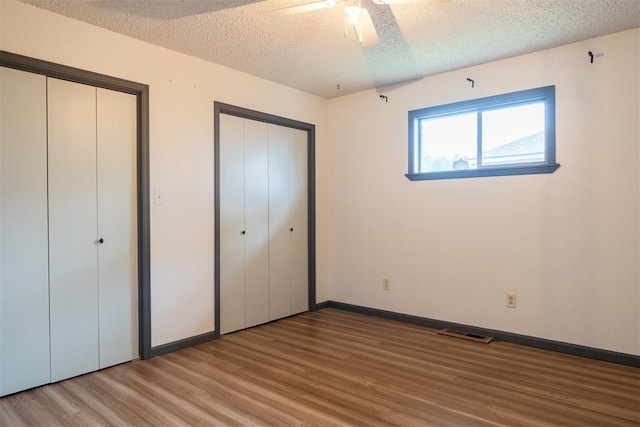 515 W Tennessee Ave, Pauls Valley, OK 73075 - unfurnished bedroom featuring wood finished floors, two closets, a textured ceiling, baseboards, and ceiling fan