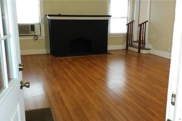 unfurnished living room featuring cooling unit, wood finished floors, and baseboards