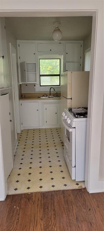 kitchen with white cabinetry, a sink, light floors, and white gas range oven