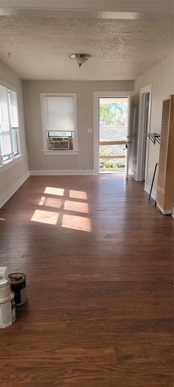 unfurnished living room featuring cooling unit, a healthy amount of sunlight, baseboards, and dark wood finished floors