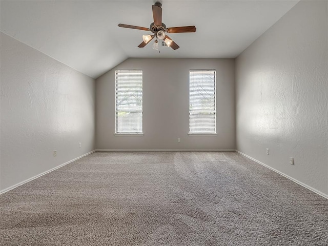 carpeted empty room with vaulted ceiling, a ceiling fan, and baseboards