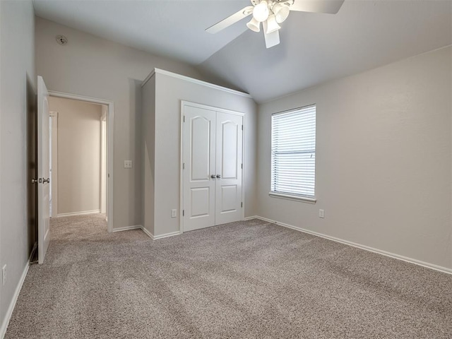 unfurnished bedroom with lofted ceiling, carpet floors, a closet, baseboards, and ceiling fan