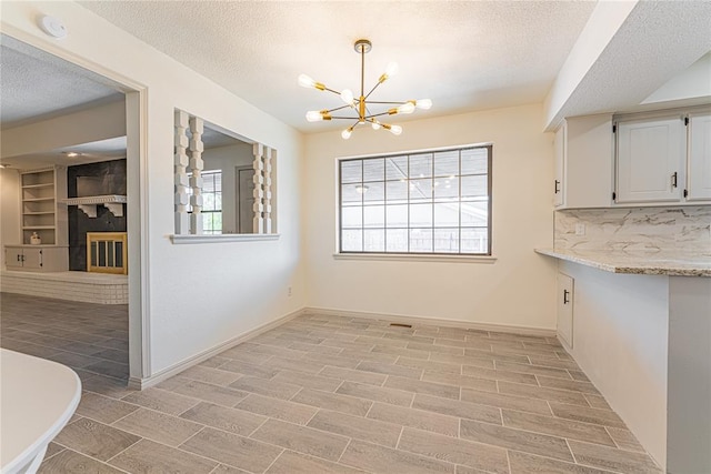 11800 Shasta Ln, Oklahoma City, OK 73162 - unfurnished dining area featuring a glass covered fireplace, light wood-style floors, a textured ceiling, and an inviting chandelier