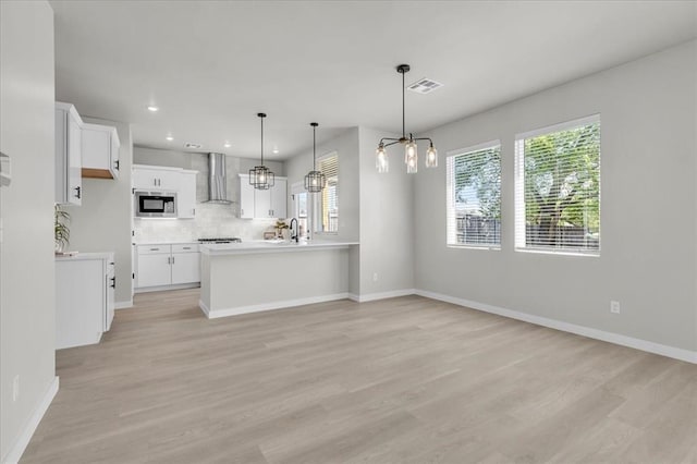 508 NW 175th St, Edmond, OK 73012 - kitchen with stainless steel microwave, wall chimney range hood, a chandelier, light wood-type flooring, and white cabinetry