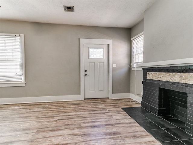 foyer entrance featuring a fireplace, a textured ceiling, visible vents, wood finished floors, and baseboards
