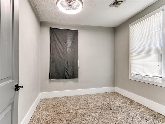carpeted empty room featuring a textured ceiling, baseboards, visible vents, and a wealth of natural light