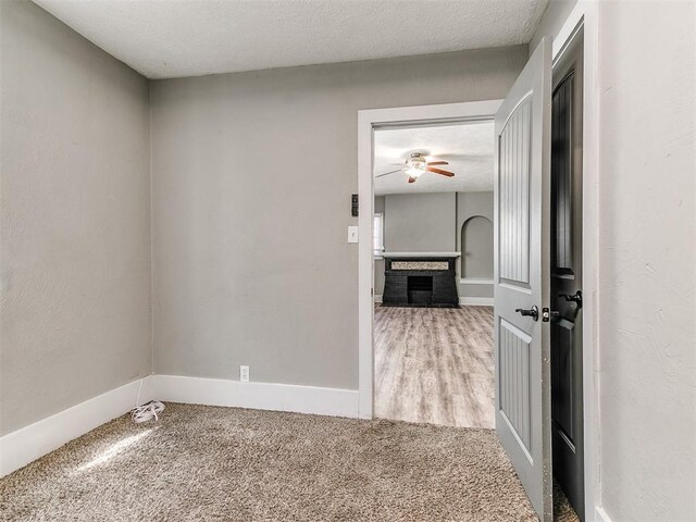 carpeted empty room featuring a fireplace, baseboards, and a ceiling fan