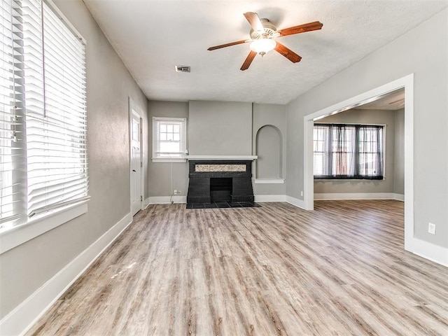unfurnished living room with baseboards, a fireplace, a ceiling fan, visible vents, and wood finished floors
