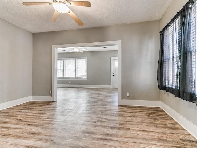 empty room featuring a textured ceiling, wood finished floors, baseboards, and a ceiling fan