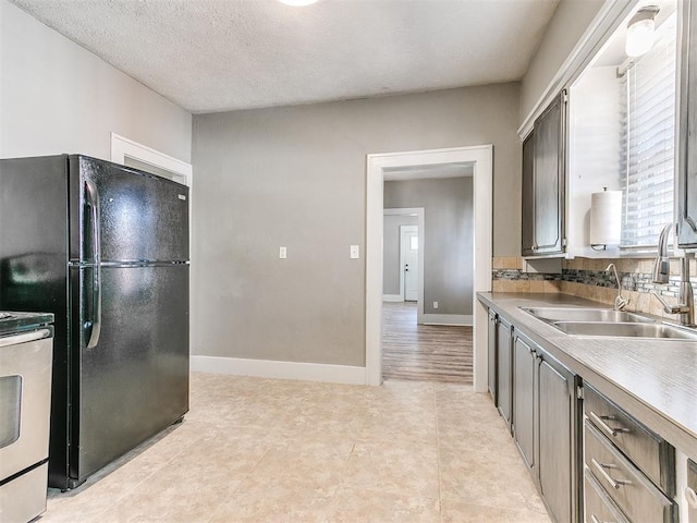 kitchen featuring baseboards, stove, freestanding refrigerator, and a sink