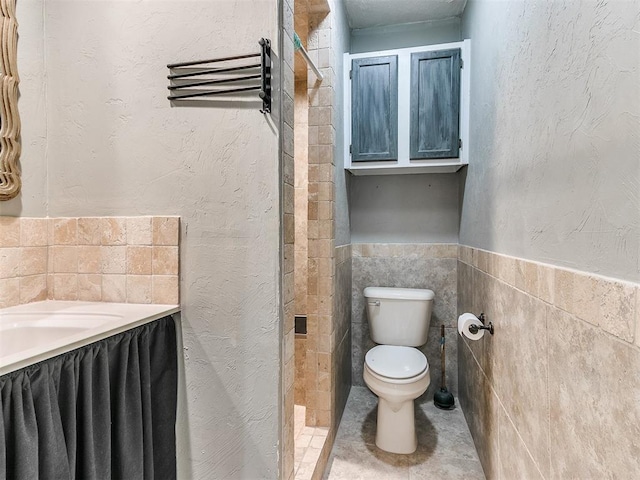 bathroom with toilet, tile patterned floors, wainscoting, and tile walls