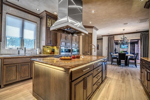 5100 Wisteria Dr, Oklahoma City, OK 73142 - kitchen featuring crown molding, visible vents, island exhaust hood, a center island with sink, and light wood finished floors