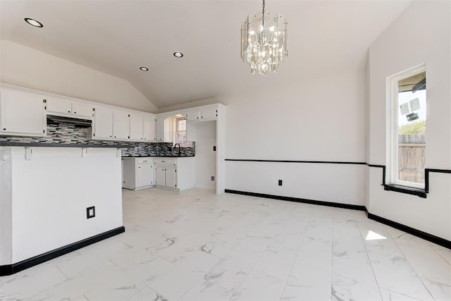 kitchen with under cabinet range hood, dark countertops, white cabinetry, a notable chandelier, and lofted ceiling