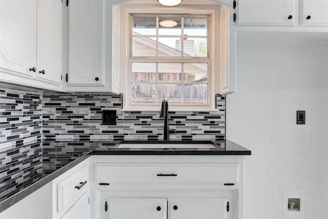 kitchen featuring dark countertops, a sink, backsplash, and white cabinetry