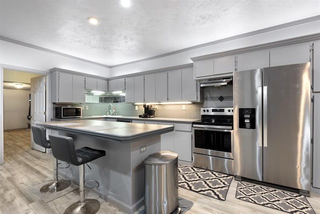 kitchen with tile counters, a center island, under cabinet range hood, light wood-style floors, and stainless steel appliances