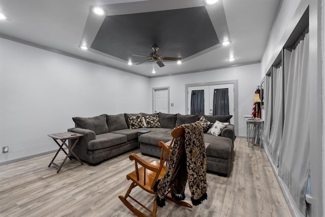 living area featuring french doors, a tray ceiling, a ceiling fan, and light wood-style floors