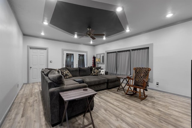 living area with light wood-style flooring, a ceiling fan, recessed lighting, a raised ceiling, and baseboards