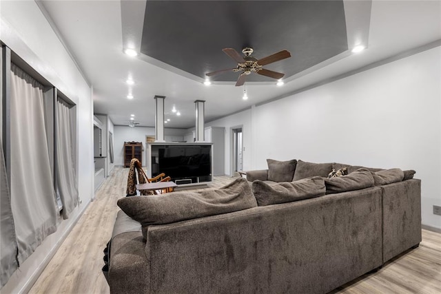 living room featuring light wood-style flooring, ceiling fan, and a raised ceiling