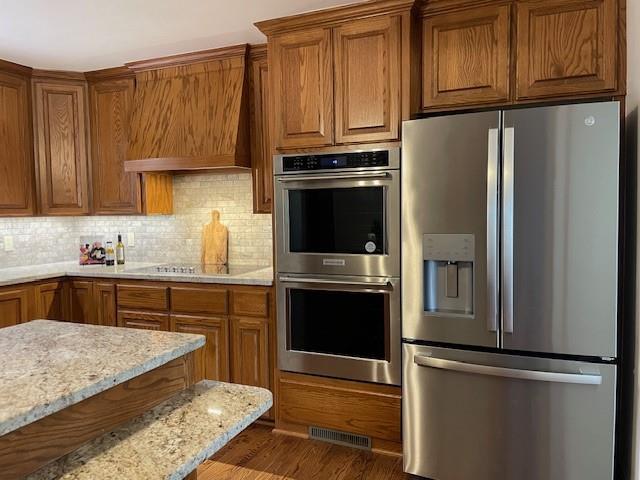 401 Memorial Dr, Okarche, OK 73762 - kitchen with custom range hood, visible vents, brown cabinetry, and stainless steel appliances