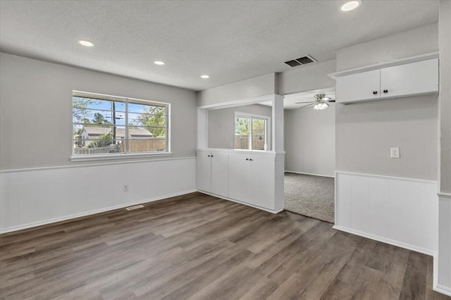 spare room with a textured ceiling, a ceiling fan, visible vents, wood finished floors, and wainscoting