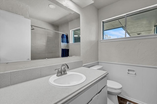 bathroom with a shower with shower curtain, vanity, a textured wall, toilet, and wood finished floors