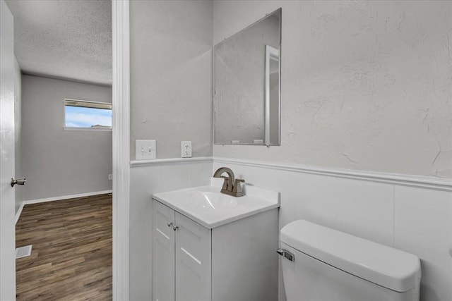 bathroom featuring toilet, a textured ceiling, wainscoting, vanity, and wood finished floors