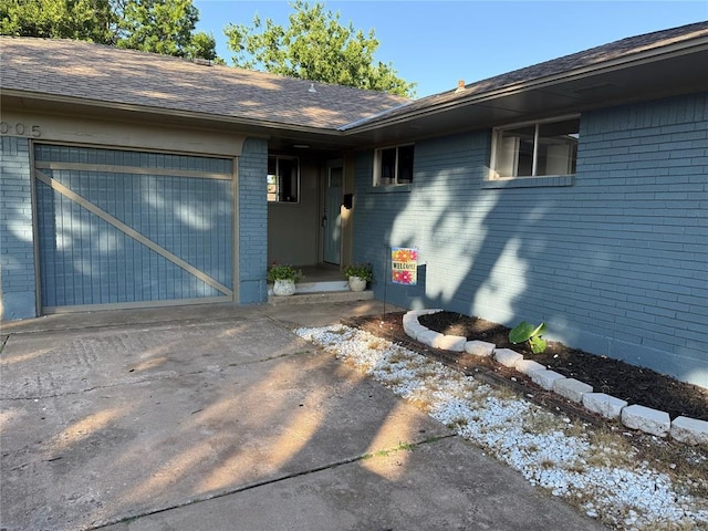 1005 W Silver Meadow Dr, Midwest City, OK 73110 - doorway to property featuring brick siding, a garage, concrete driveway, and a shingled roof