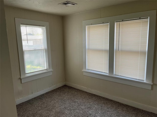 carpeted spare room featuring a wealth of natural light, visible vents, and baseboards